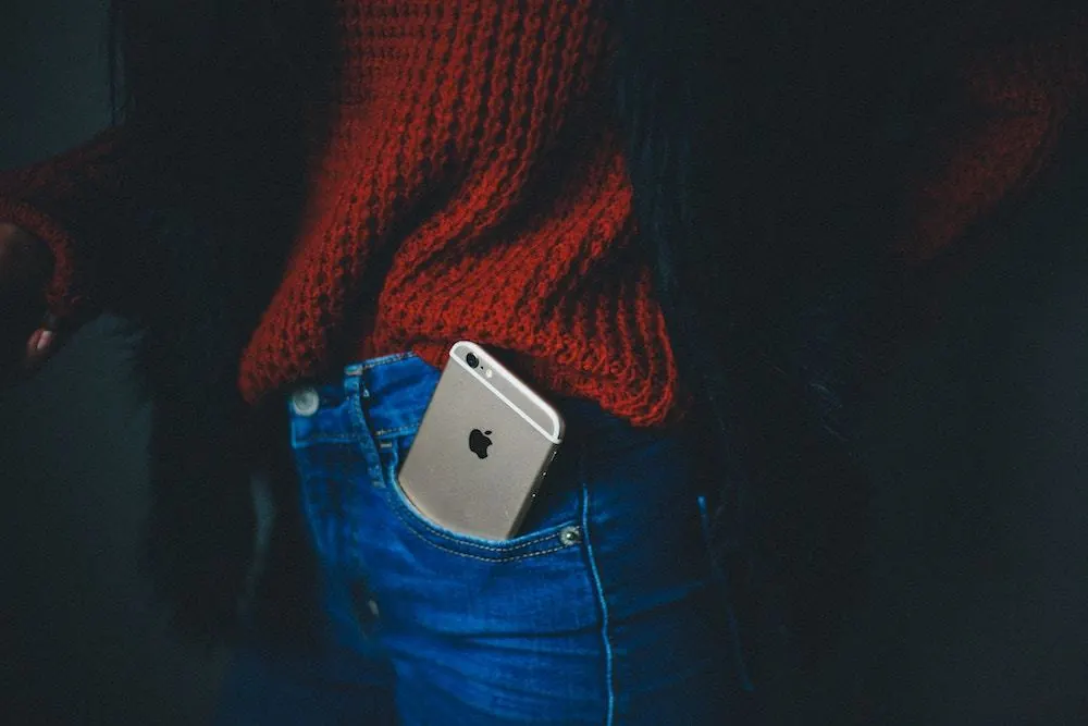 A woman wearing jeans and a red sweater with an iphone in her pocket.