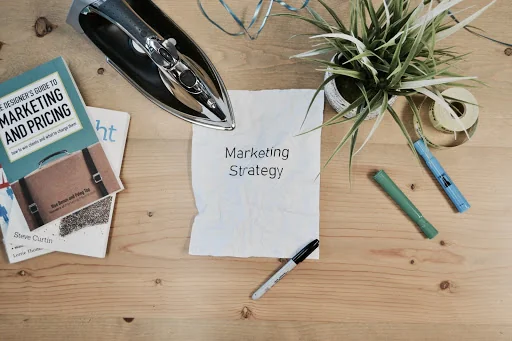 A note with the word marketing strategy on it sits on a wooden table.