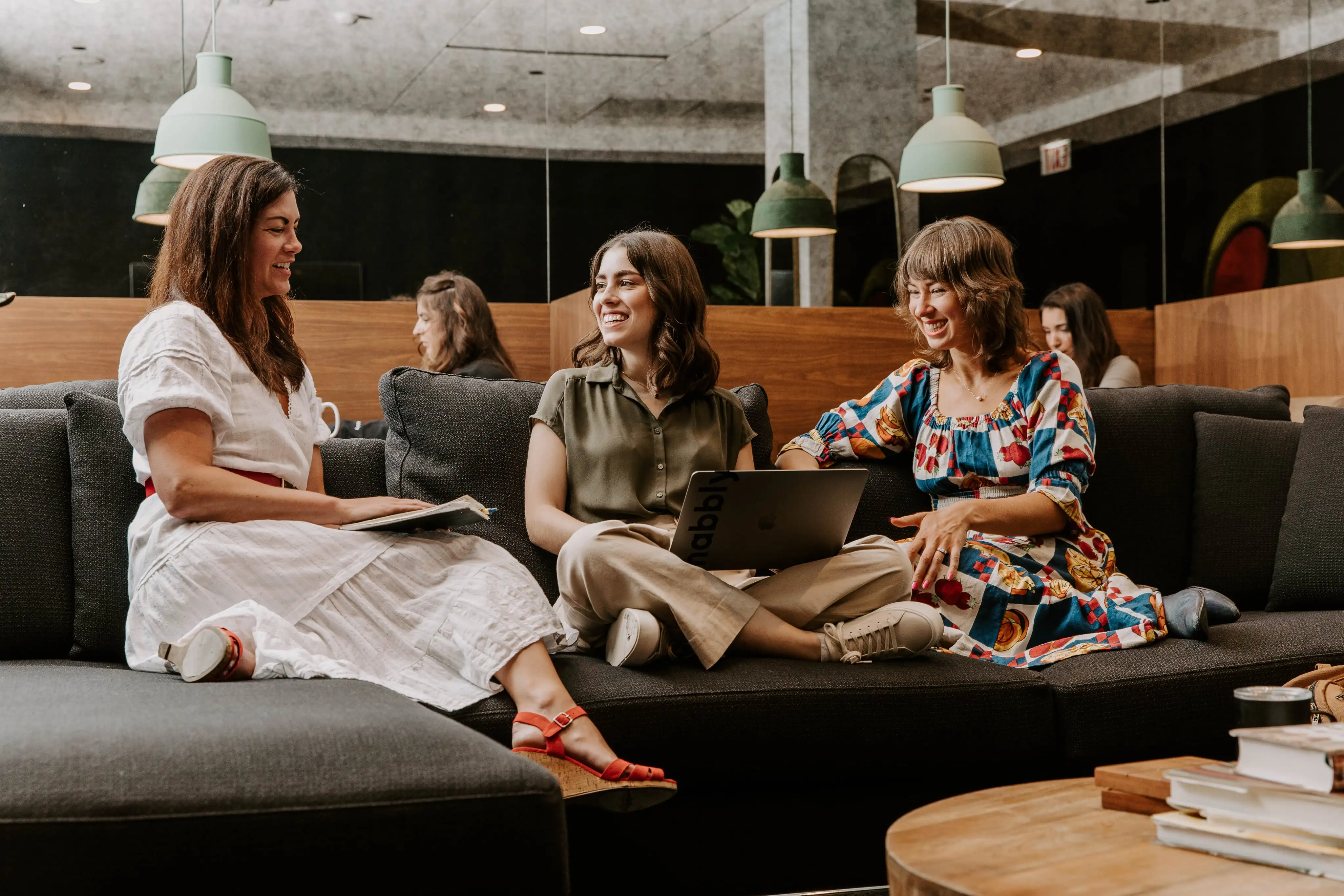 Three women sitting on a couch with laptops.