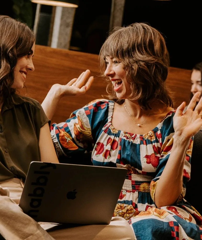 Two women sitting on a couch, working on laptops for a digital marketing agency.