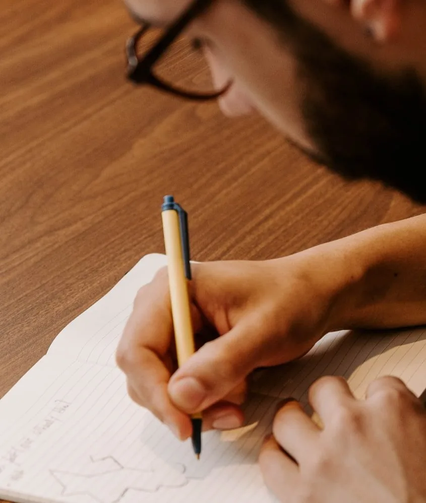 A man, employed by a digital marketing and branding agency, diligently writes in a notebook with a pen.